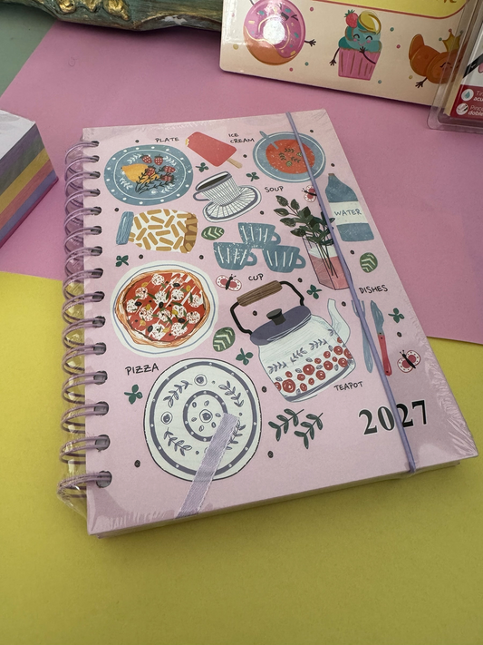 Agenda Brena 2027 de espiral en color rosa con ilustraciones de comida y cocina sobre fondo rosa y amarillo