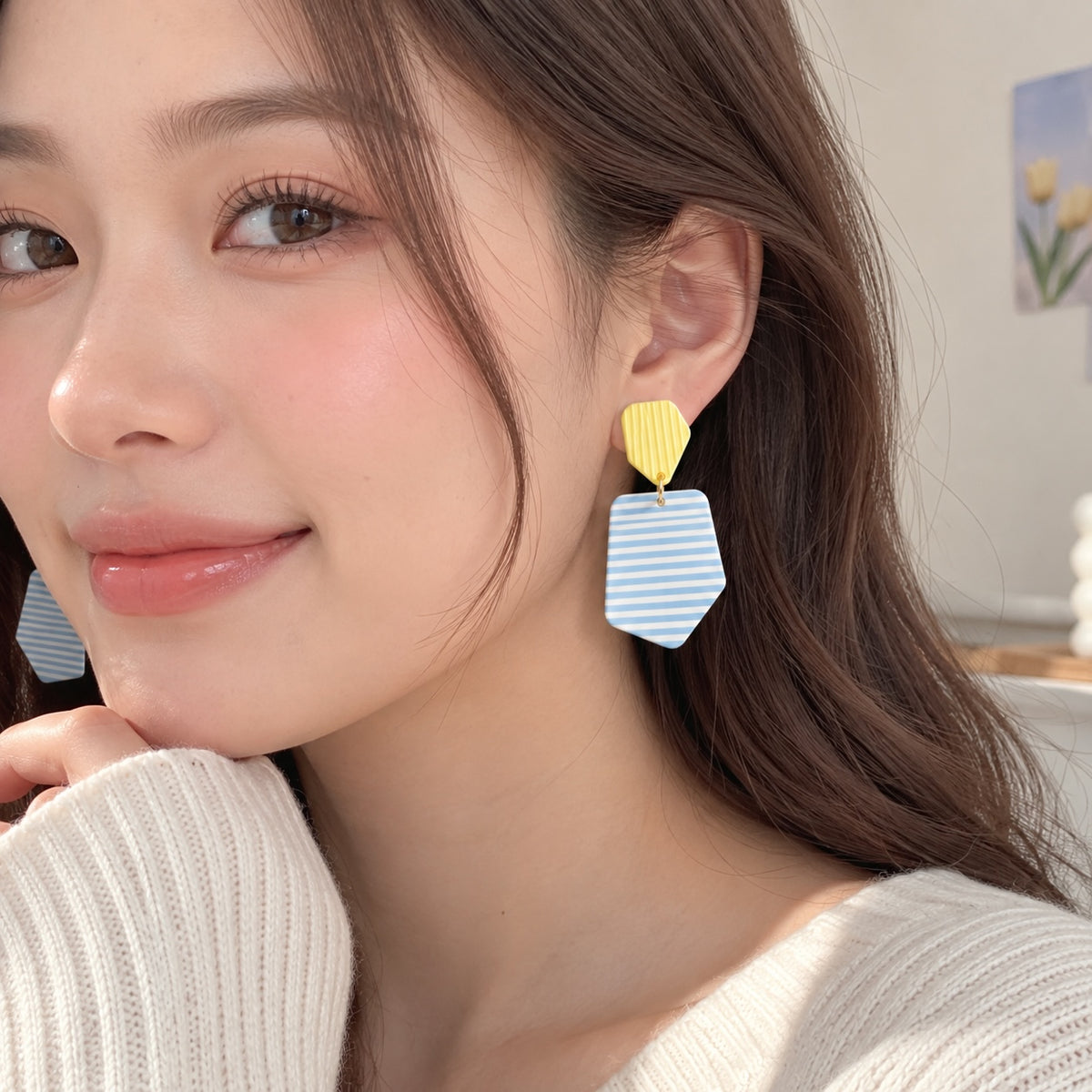 Mujer luciendo aros colgantes Brena geométricos con pieza superior amarilla estriada y colgante azul y blanco a rayas