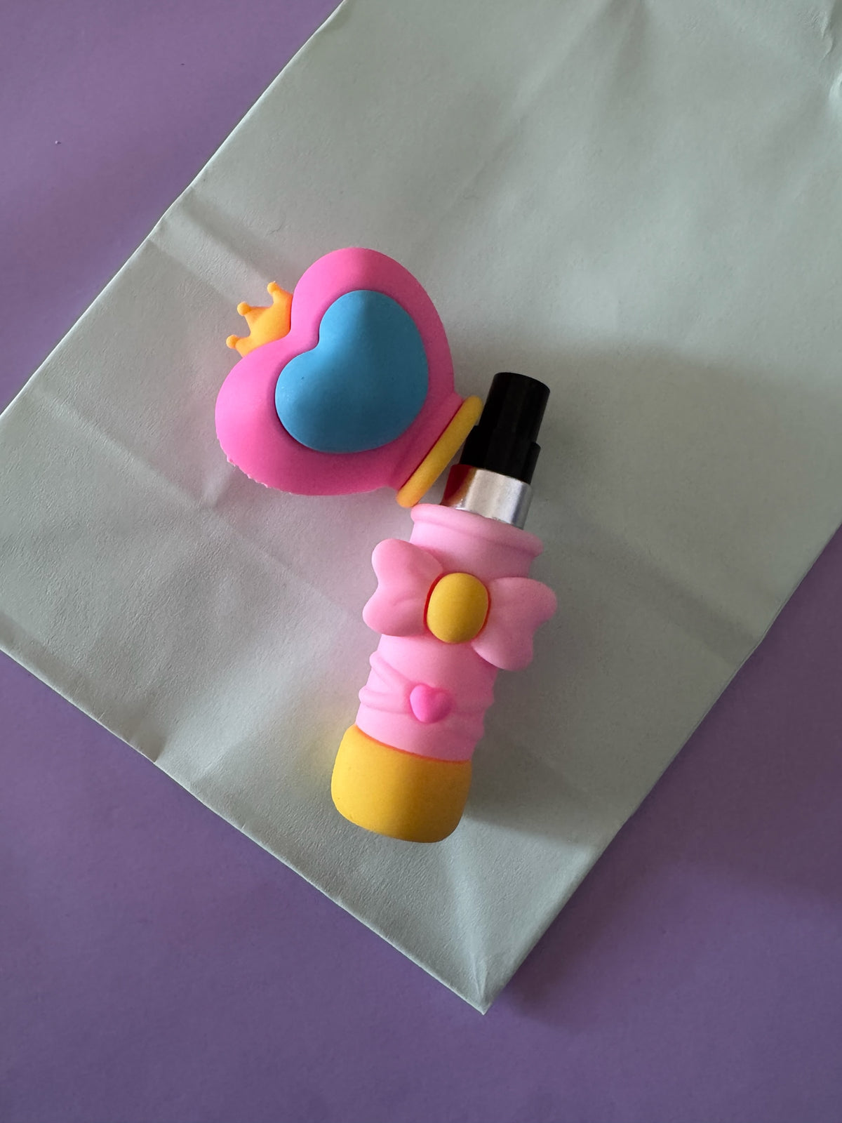 Atomizador de perfume Brena con diseño de varita mágica en colores rosa, azul y amarillo con detalles de lazo y corona.