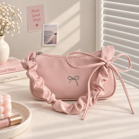 Bolso de hombro Brena rosa pastel tipo baguette con correa fruncida, detalle de lazo metálico y cierre de cremallera.