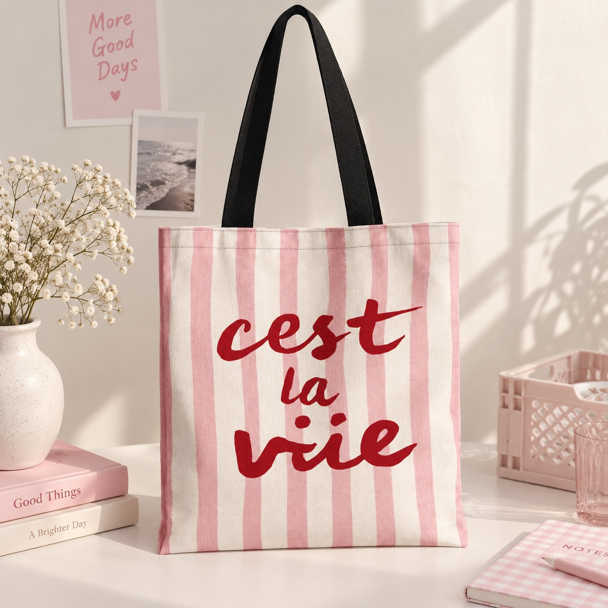 Bolso tote Brena de lona con rayas rosa y blanco, estampado rojo cest la vie y asas negras sobre mesa decorada.
