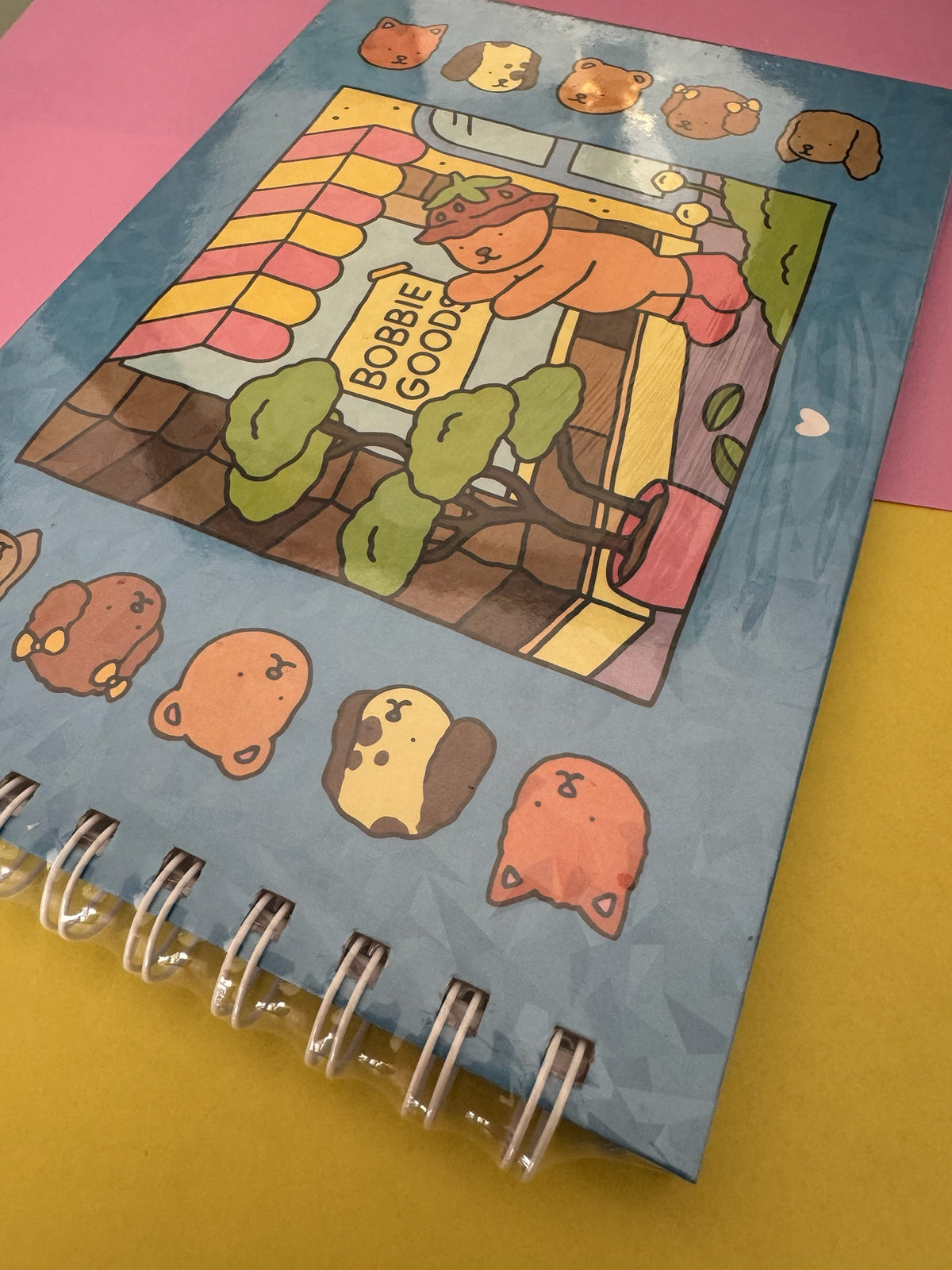 Cuaderno de espiral Brena con ilustración kawaii de ositos y tienda en portada sobre fondo azul y amarillo