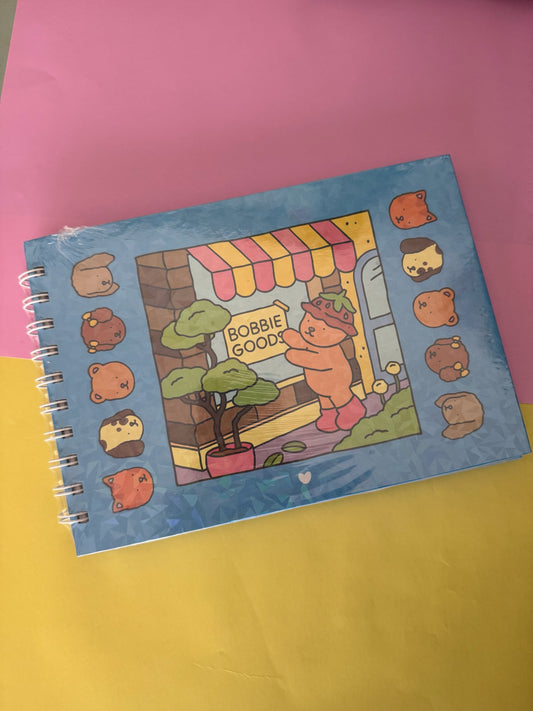Cuaderno de espiral Brena con diseño kawaii de oso y tienda, formato horizontal ideal para notas y bocetos.