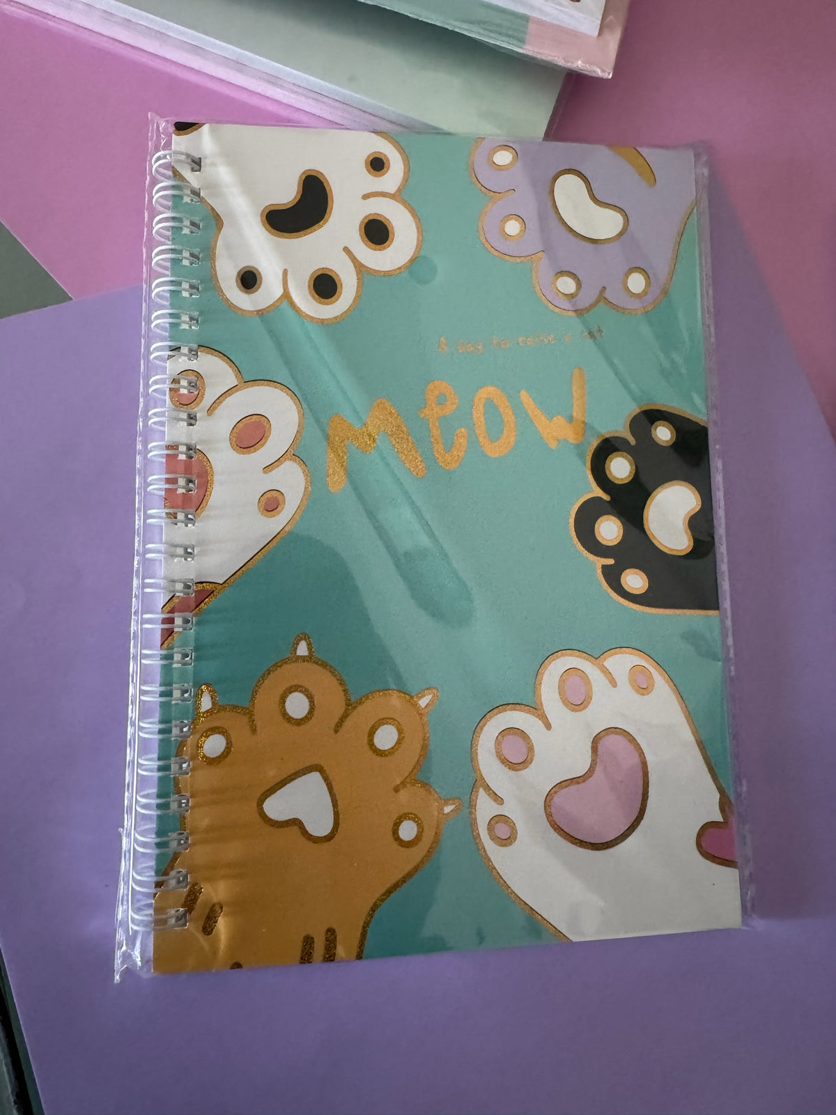 Cuaderno Brena de espiral con portada turquesa, estampado de huellitas y texto brillante meow para notas escolares