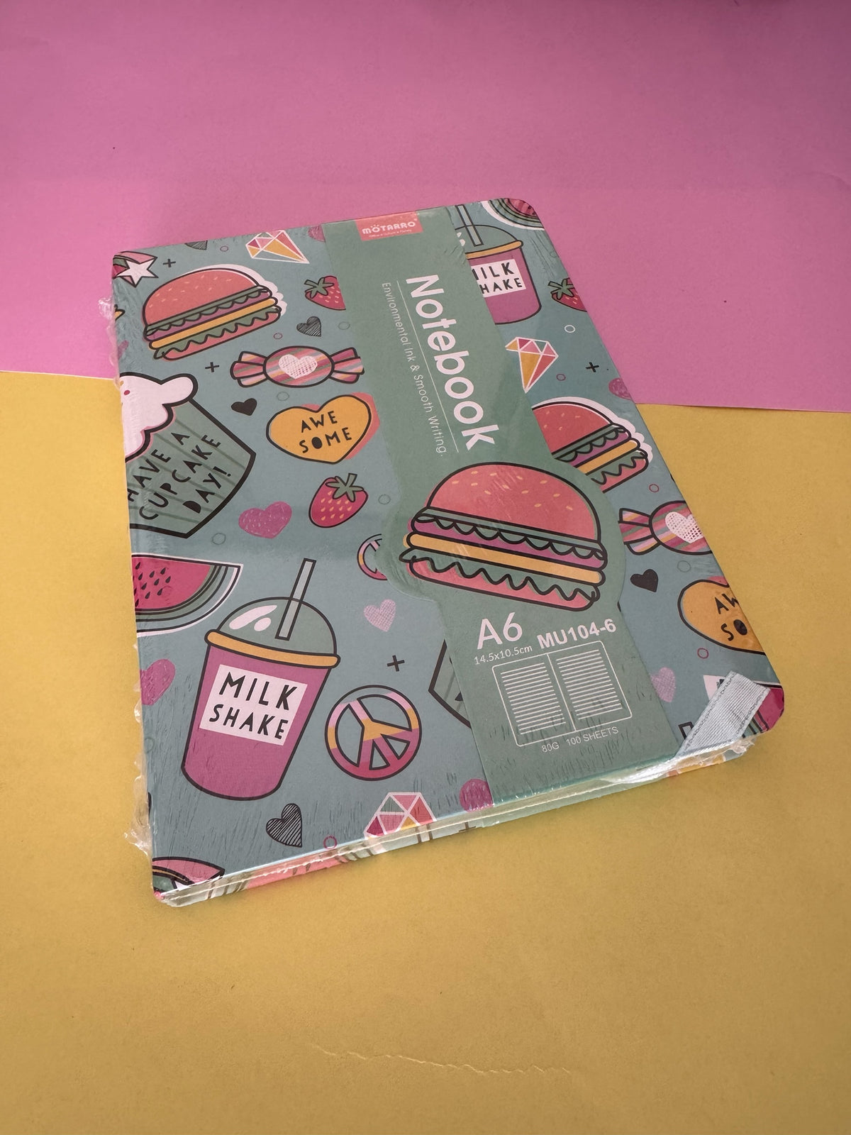 Cuaderno Brena tamaño A6 con estampado colorido de hamburguesas y batidos sobre fondo verde agua.