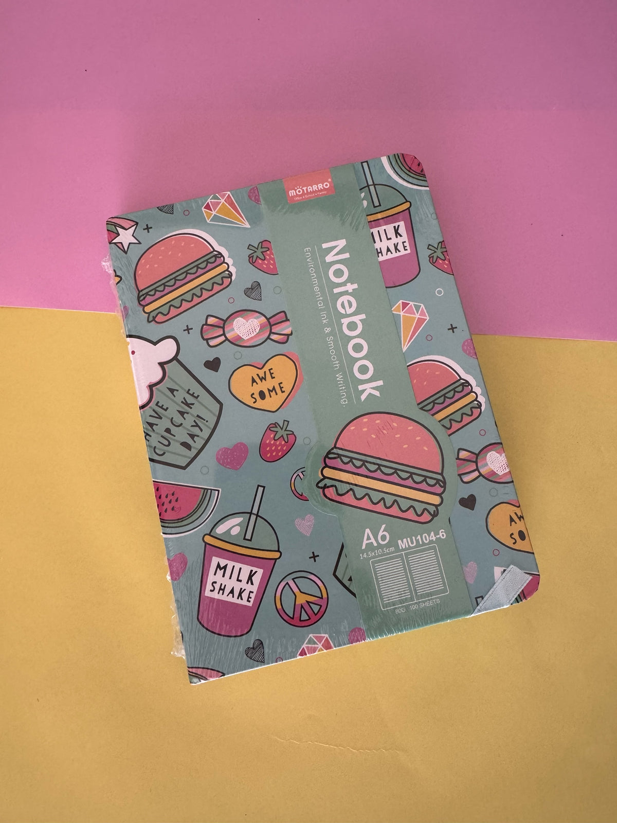 Cuaderno Brena tamaño A6 con estampado colorido de hamburguesas y batidos sobre fondo verde agua.