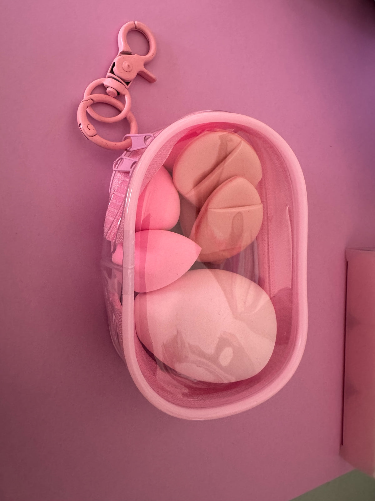 Estuche transparente Brena con esponjas de maquillaje rosadas de diversas formas y gancho mosquetón para viaje