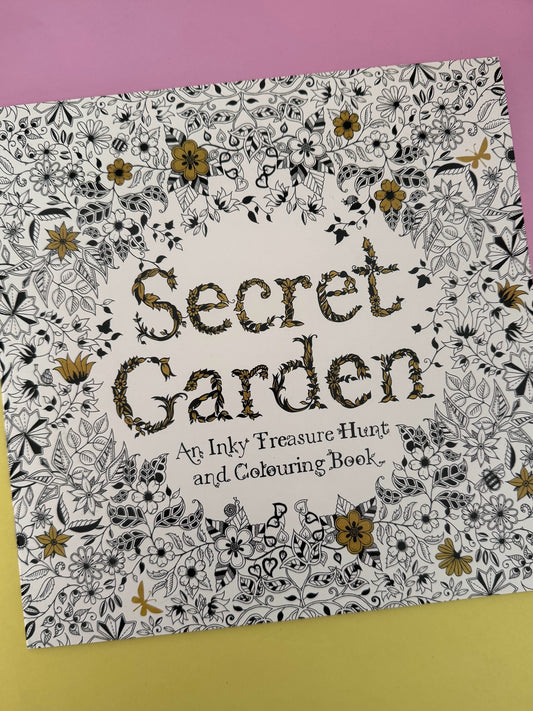 Libro de colorear Brena Secret Garden con ilustraciones botánicas detalladas en blanco, negro y toques dorados.