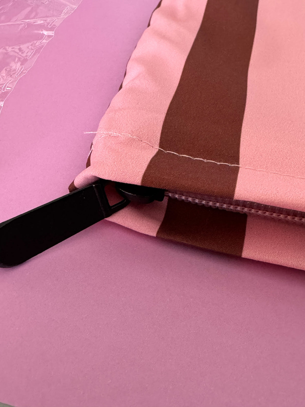 Neceser Brena de tela a rayas rosas y marrones con cierre negro, ideal para organizar accesorios personales.