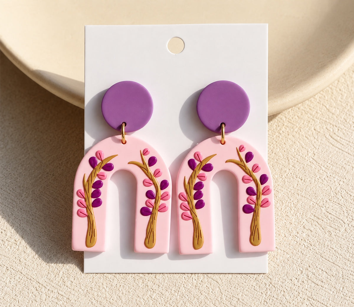 Pendientes Brena de arcilla polimérica en forma de arco, color rosa con diseño botánico púrpura y dorado en relieve.