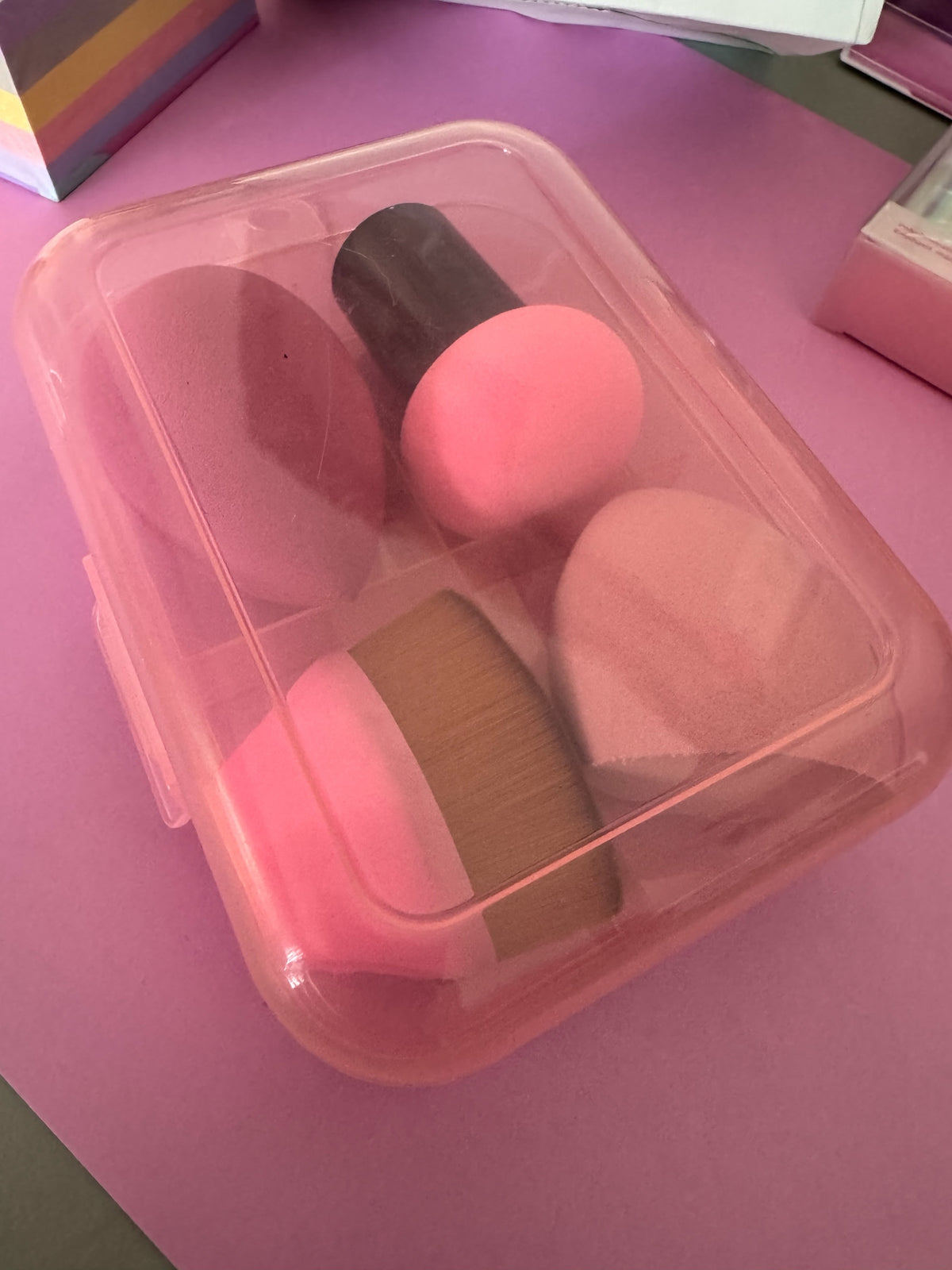 Set de esponjas y brocha de maquillaje Brena en tonos rosados dentro de un estuche protector de plástico traslúcido.